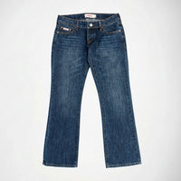A pair of medium-wash blue denim Bubblegum jeans with the Nola super low rise, flare leg, laid flat against a light gray background.