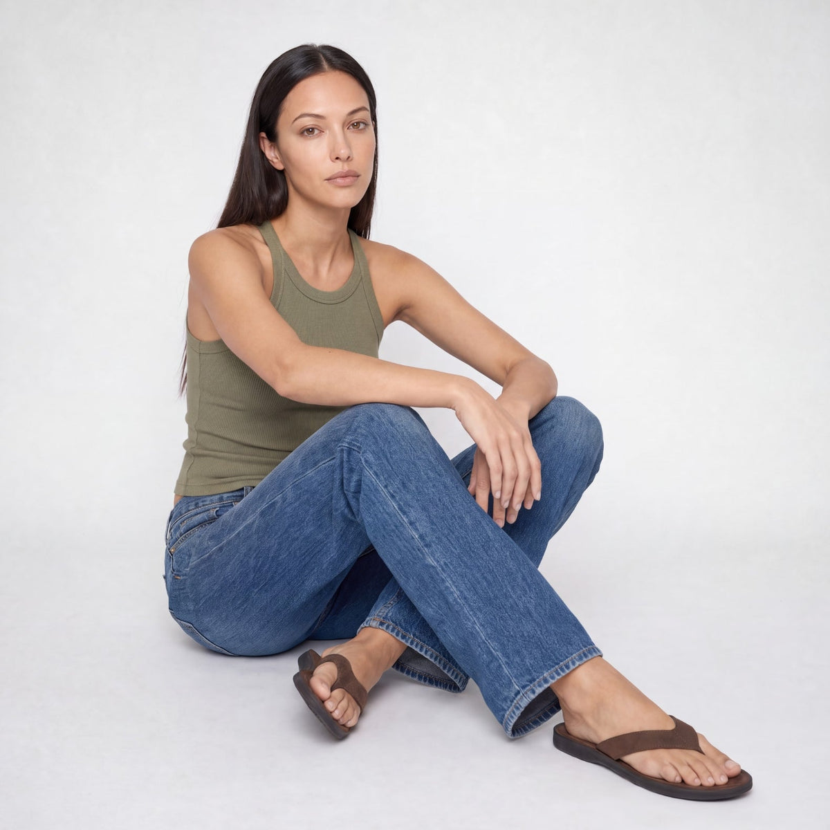Lisa model sitting on the floor wearing a green tank top and a blue indigo Bubblegum Jeans on a white background