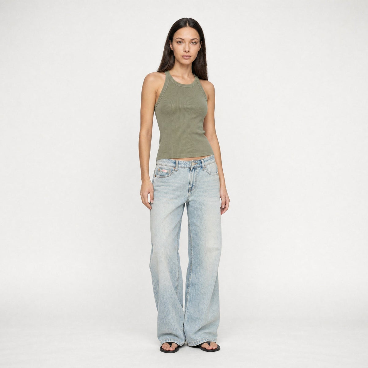 A model wearing a green tank top with light indigo denim wash Bubblegum jeans posing in front of a white background.