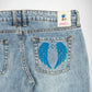 Close-up of the back of light-wash blue denim Bubblegum jeans showing a large embroidered pair of bright blue wings on the back pocket, with a visible Bubblegum brand label at the waistband.