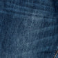 A close-up of dark blue denim fabric showing the detailed twill weave texture and a subtle yellow-orange contrast stitch in the bottom right corner.