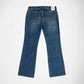 Back view of a pair of blue denim jeans with a star-shaped stud embellishments details on the back pocket, photographed flat on a white background.
