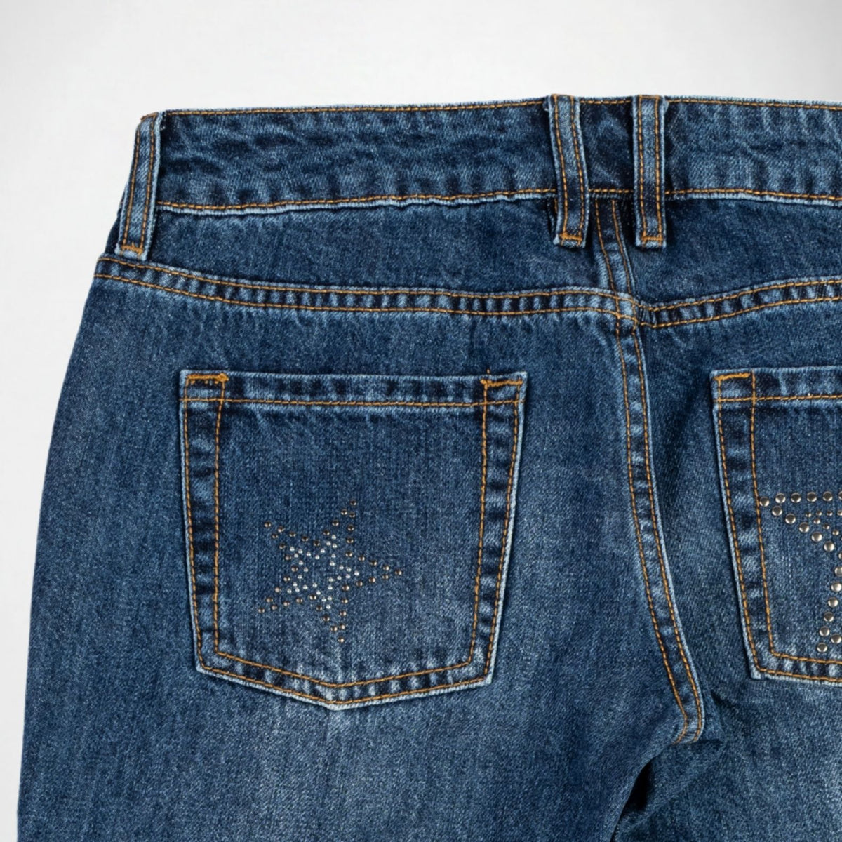 Close-up of the back of blue denim Bubblegum jeans showing the waistband, belt loops, and back pockets with star-shaped stud embellishments on a white background.