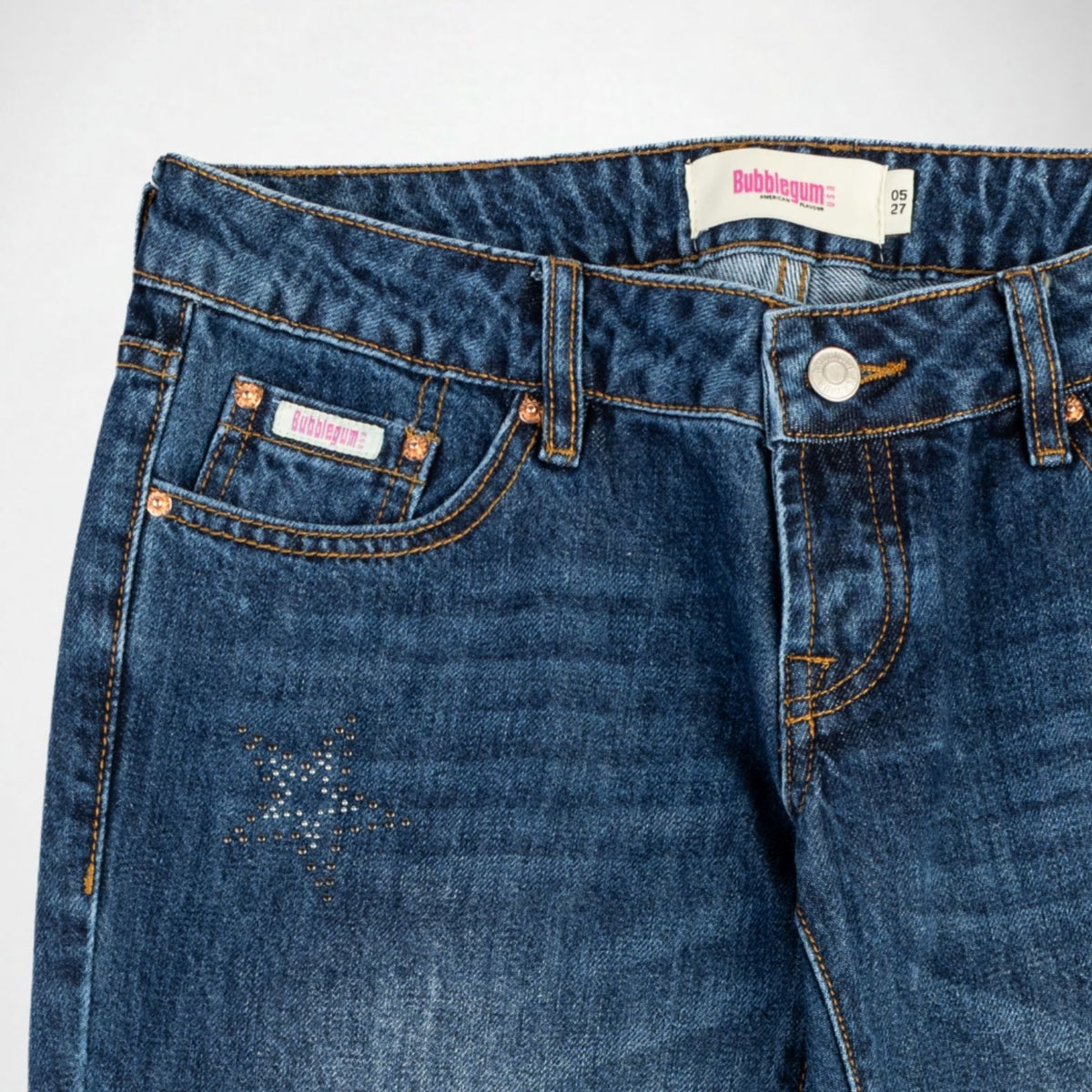 Close-up of a pair of blue denim Bubblegum jeans showing the front waistband, button closure, pocket details, with star-shaped stud embellishments on the left thigh. The brand label 'Bubblegum USA' is visible on the inner waistband and pocket.