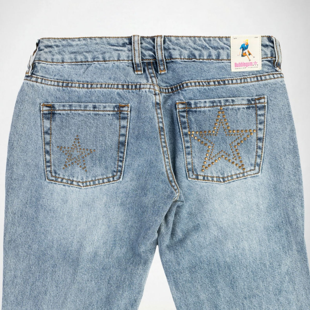 Back view of light-wash blue Bubblegum jeans featuring large star-shaped embellishments on both back pockets, with a visible Bubblegum USA brand label at the waistband.