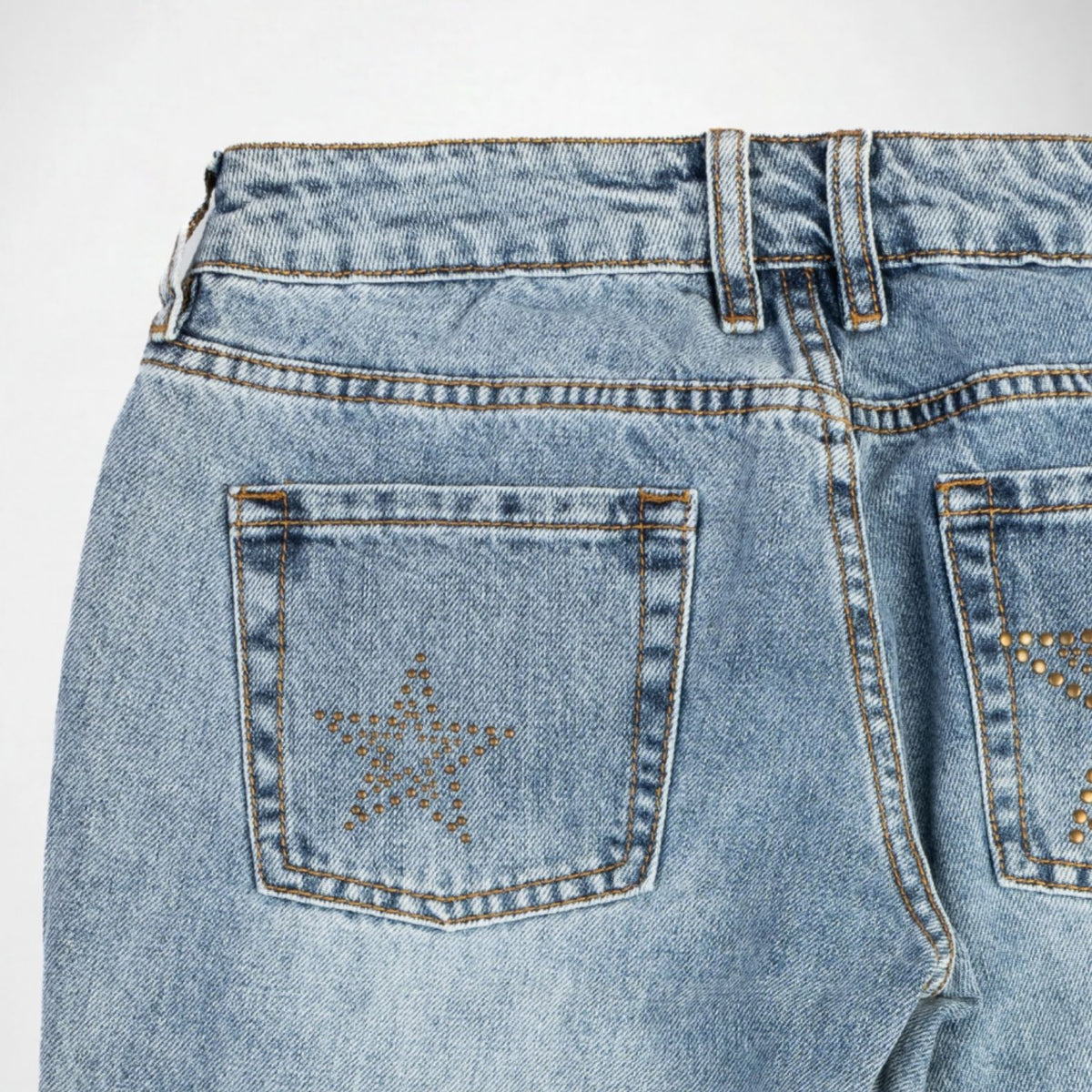 Close-up back view of light blue denim Bubblegum jeans showing the waistband, belt loops, and back pockets with decorative metallic star embellishments on a white background.