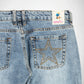 Close-up back view of light-wash blue denim Bubblegum jeans showing the waistband, belt loops, back pockets, and a large star-shaped stud embellishment outlined in gold on the right pocket. A Bubblegum USA brand patch is visible at the back waist.