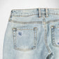 Close-up of the back waistband and rear pockets of light-wash blue denim Bubblegum jeans, showing embroidered cherry blossom flower details in indigo and white color thread, on the back pockets and contrast stitching.