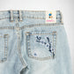 Close-up back view of light-wash denim Bubblegum jeans showing the back pocket with embroidered blue and white cherry blossom flower detail, plus a visible 'Bubblegum USA' label at the waistband.