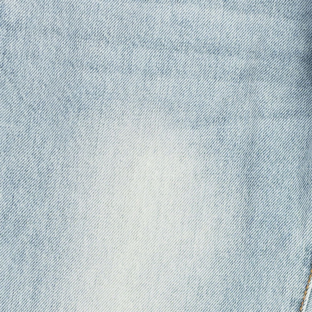 A close-up of light blue denim fabric with a subtle white faded area in the center and visible diagonal twill texture.