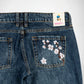 Close-up back view of dark blue denim Bubblegum jeans with embroidered Pink and white cherry blossoms on the right pocket. A sewn-on 'Bubblegum USA' brand patch is visible at the waistband.