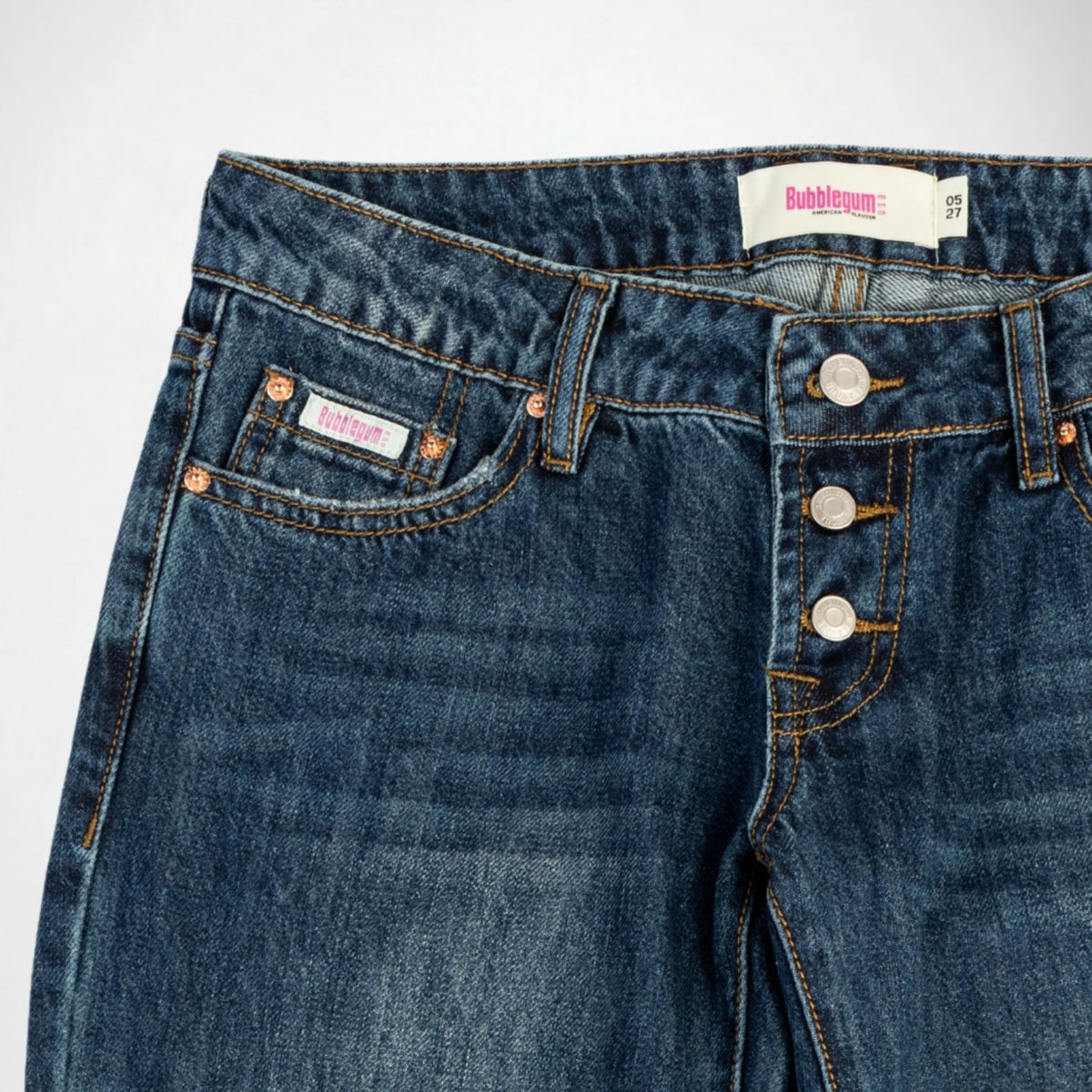 Close-up of dark blue denim Bubblegum jeans showing the waistband, button fly, front pockets, and a visible Bubblegum USA brand label.