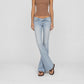 A model wearing the Rose super low rise flare in light indigo vintage wash bubblegum jeans, a brown ribbed tank top, and dark brown sandals, standing against a light gray studio background.