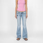 A model wearing the Nola super low flare in light-wash blue denim Bubblegum jeans with a shadow & stud embellished star on the left thigh, paired with a pink tank top and black sandals, against a plain white studio background.
