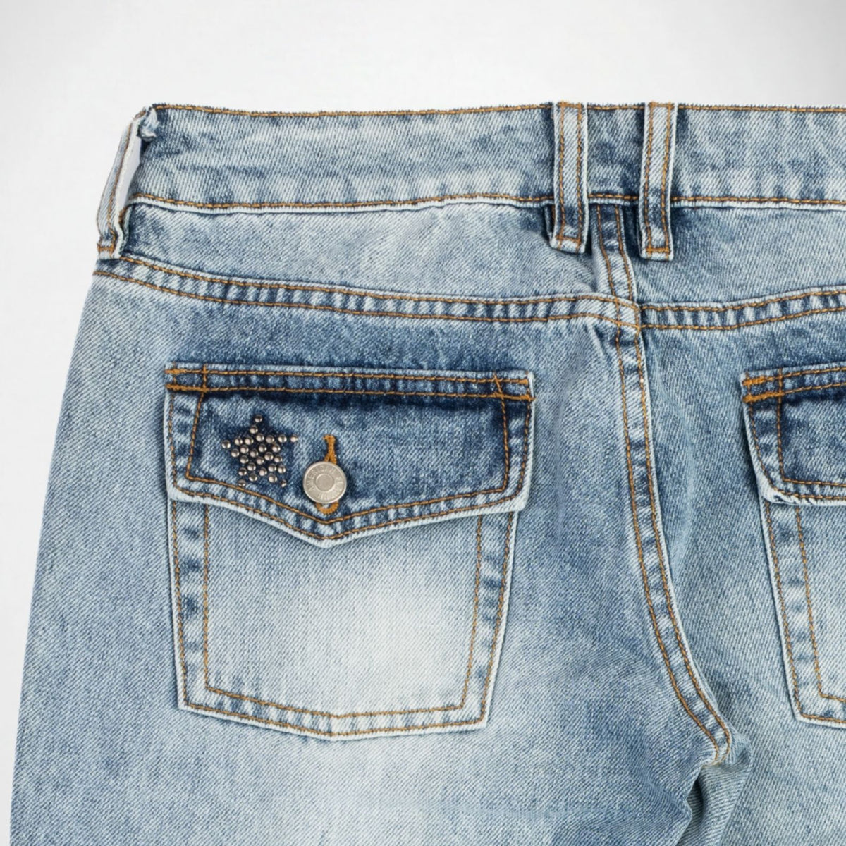 Close-up back view of light-wash blue denim Bubblegum jeans showing the waistband, belt loops, and back pockets with silver stud metallic embellished details.