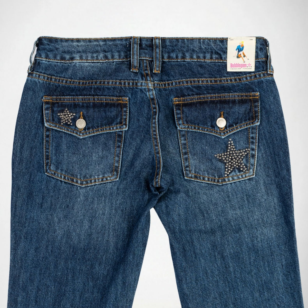 Back view of blue denim Bubblegum jeans featuring star-shaped pocket embellishments with studs and silver buttons on the back pockets, with a visible Bubblegum USA brand tag at the waistband.