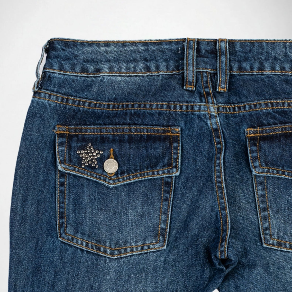 Close-up back view of blue denim Bubblegum jeans showing the waistband, belt loops, and back pockets with silver studs star-shaped embellishment on the left pocket.