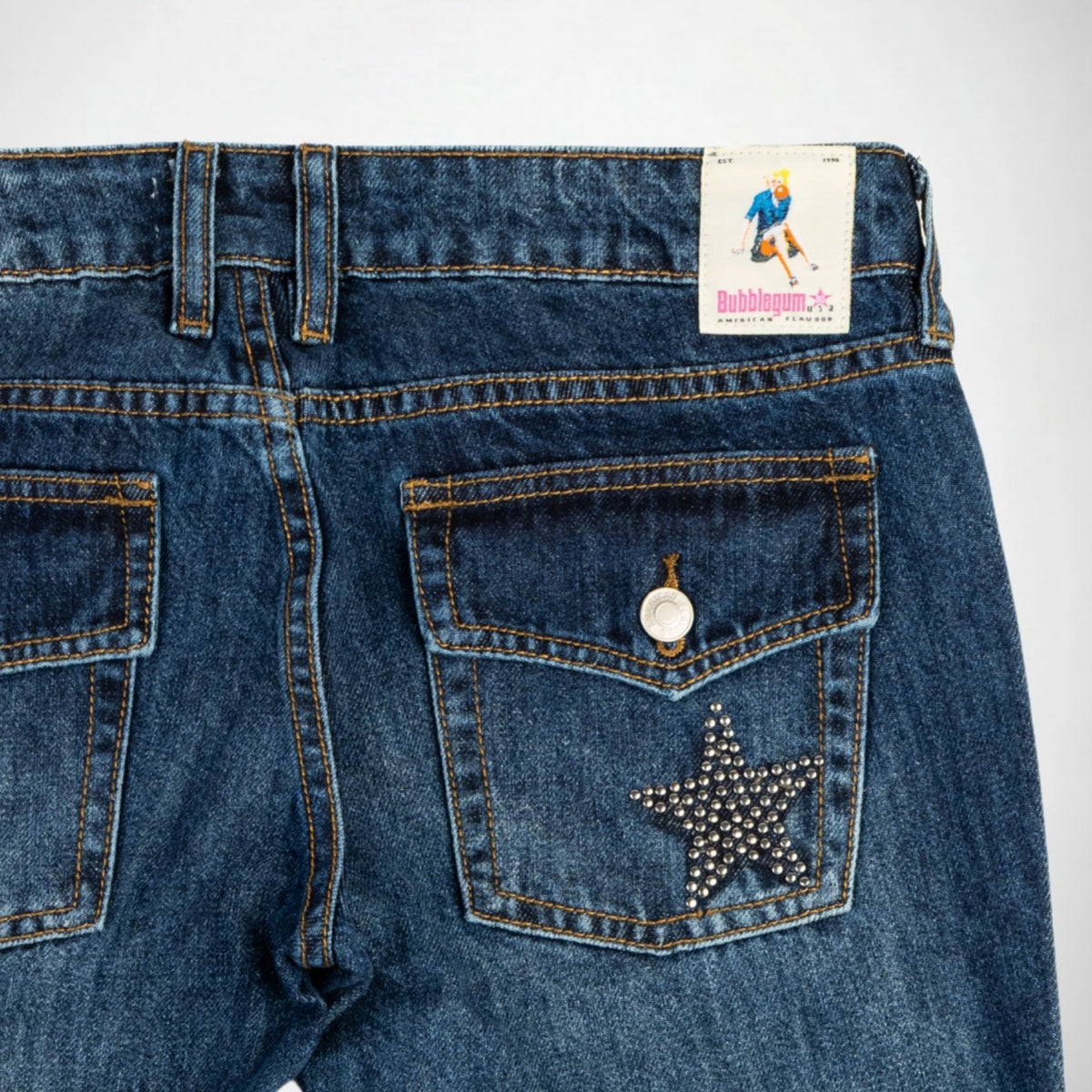 Close-up back view of dark blue denim Bubblegum jeans showing the waistband, belt loops, back pockets, and a stud-embellished star on the right pocket. A patch brand label reading Bubblegum USA is visible at the waistband.
