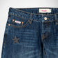Close-up of dark blue denim Bubblegum jeans showing the front waistband, button, belt loops, front pockets, and a silver star studs embellishment on the pocket. The inner label reads 'Bubblegum USA'.