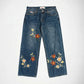 Blue denim Bubblegum jeans with colorful floral embroidery on the legs, displayed flat against a light gray background.