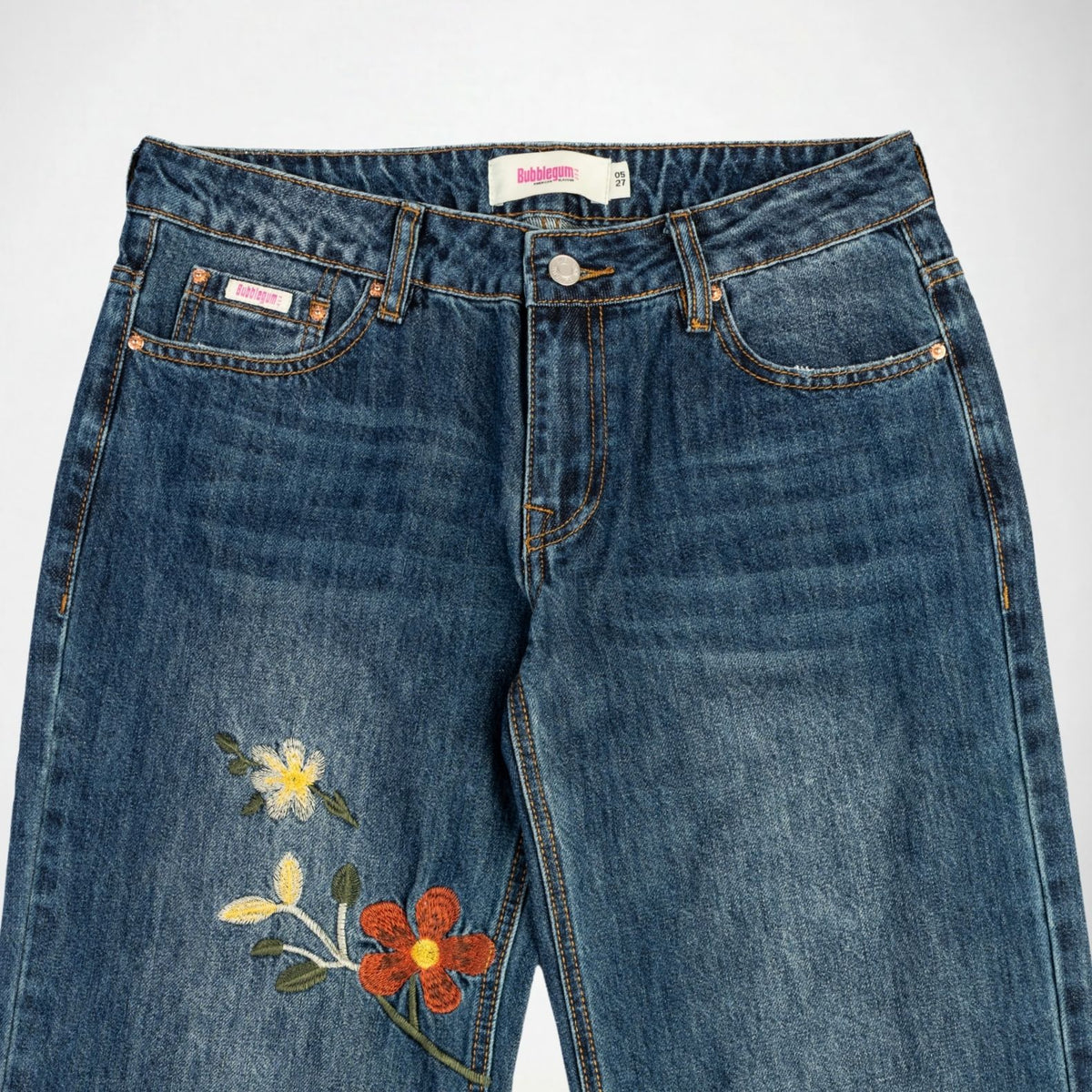 A pair of blue denim Bubblegum jeans featuring embroidered flowers on the left leg, photographed flat against a light gray background.