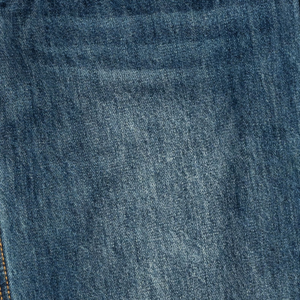 A close-up texture shot of medium-wash blue denim fabric, showing the detailed twill weave and subtle fading.