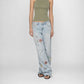 A model wearing the Lisa low baggy wide, mid rise in light-wash Bubblegum wide-leg denim jeans with colorful floral embroidery on the legs, paired with an olive green halter top and black sandals, against a plain white studio background.