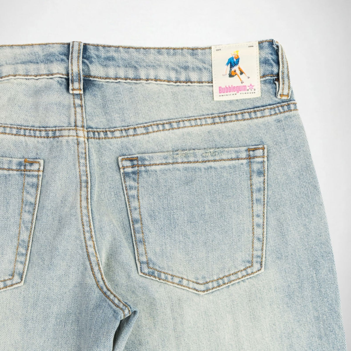 Close-up back view of light-wash blue denim Bubblegum jeans showing the waistband, belt loops, back pockets, and a visible Bubblegum USA brand patch.