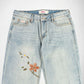 Light-wash blue denim Bubblegum jeans with floral embroidery on the left leg, featuring a white and yellow flower and a coral-orange flower with green leaves, shown against a plain white background.