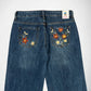 Back view of blue denim Bubblegum jeans with colorful floral embroidery on both back pockets, shown against a plain white background.