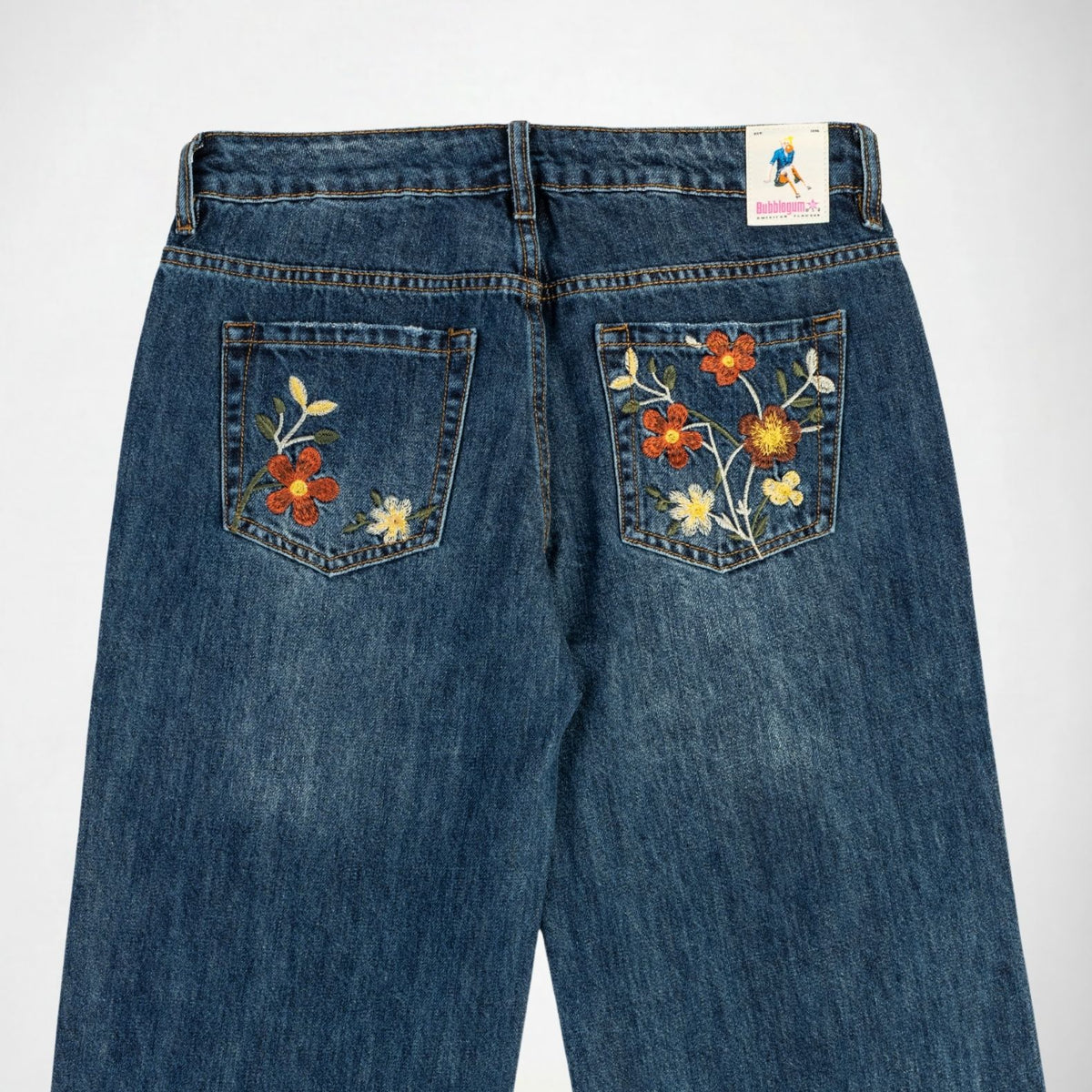 Back view of blue denim Bubblegum jeans with colorful floral embroidery on both back pockets, shown against a plain white background.