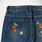 Close-up of the back pockets of blue denim Bubblegum jeans featuring embroidered floral designs in red, yellow, and green on the back pocket.