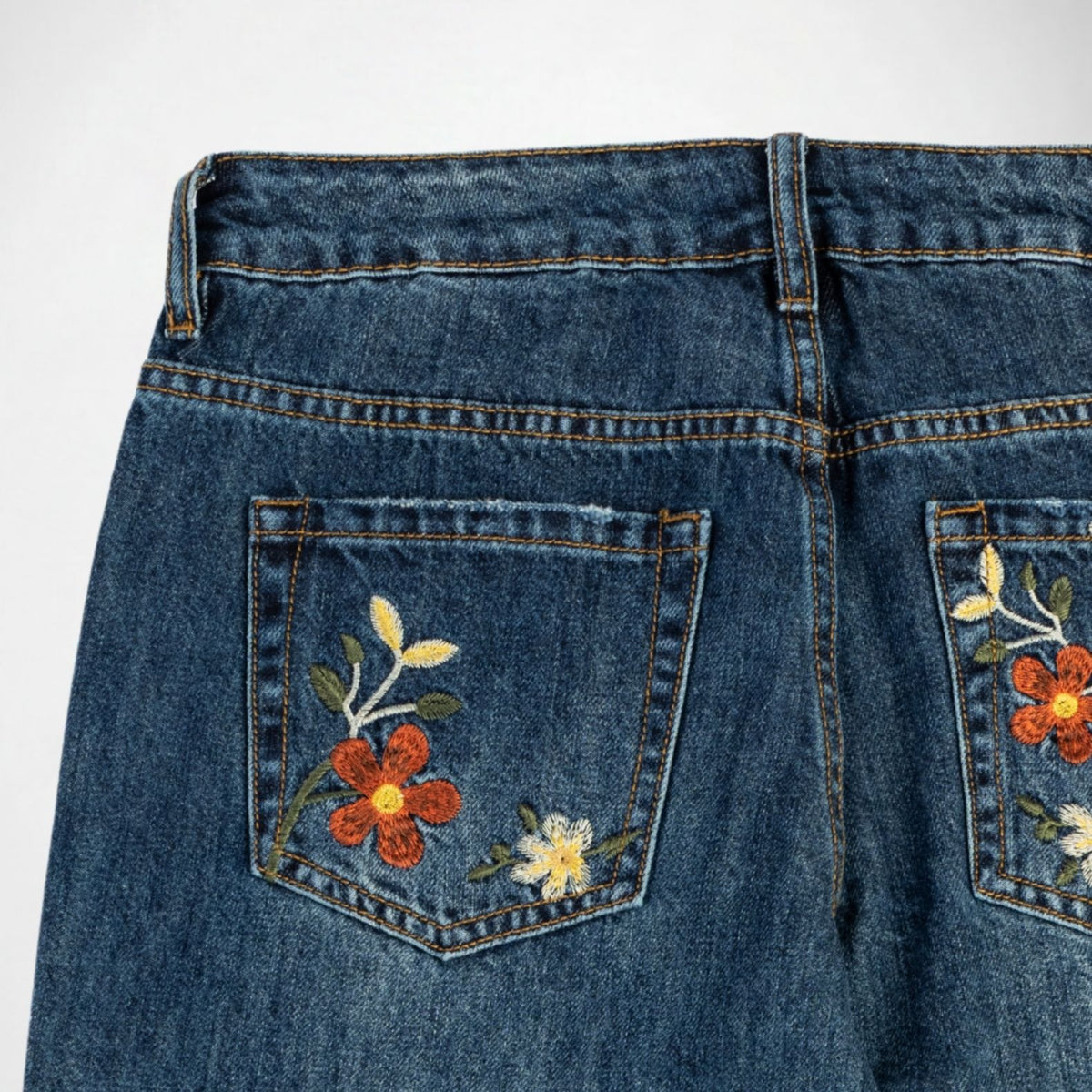 Close-up of the back pockets of blue denim Bubblegum jeans featuring embroidered floral designs in red, yellow, and green on the back pocket.