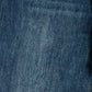 A close-up of dark blue denim fabric texture with subtle tonal variation and a small portion of contrasting stitching visible at the lower right edge.