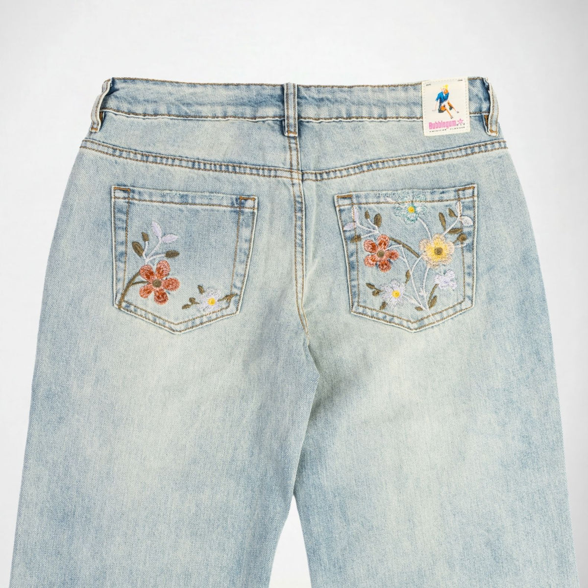 Back view of light-wash blue Bubblegum jeans featuring colorful floral embroidery on both back pockets, with a Bubblegum USA brand patch on the waistband.