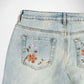 Close-up of the back pockets of light-wash blue denim Bubblegum jeans featuring embroidered floral designs in orange, green, and white.