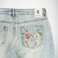 Close-up back view of light-wash denim Bubblegum jeans with floral embroidery on the back pocket. A Bubblegum USA brand patch is visible near the waistband.