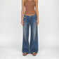 A model wearing the Luna super low wide in indigo dirty vintage wash, wide-leg Bubblegum jeans, a brown ribbed tank top, and brown sandals, standing against a light gray studio background.
