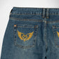 Close-up back view of blue denim Bubblegum jeans showing the back pockets with gold wing-and-heart embroidery and rhinestone detailing.