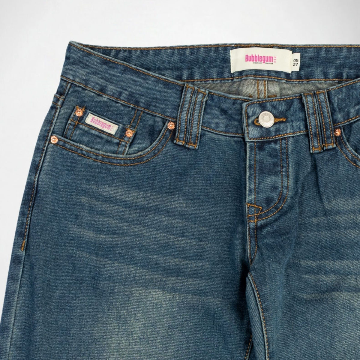 Close-up of a pair of blue denim Bubblegum jeans showing the front waistband, double belt loops, button closure, and front pockets with copper-toned rivets and contrast stitching. A visible label reads Bubblegum USA.