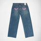 Back view of a pair of blue denim Bubblegum jeans with pink embroidered winged with rhinestones on both back pockets, shown flat against a white background.