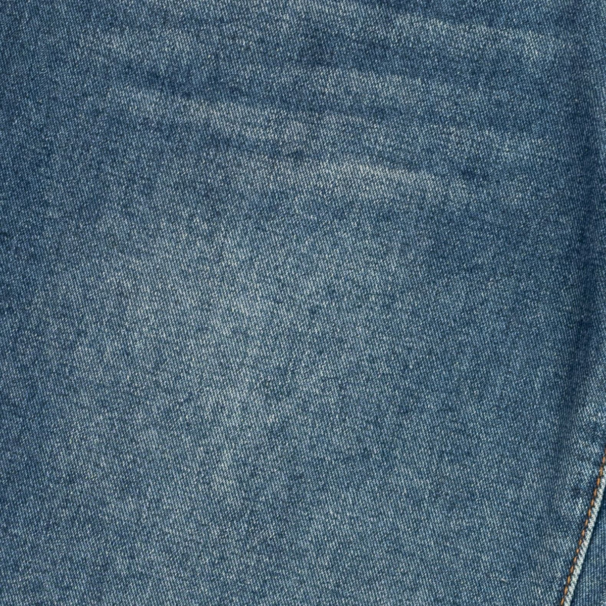 A close-up of blue denim fabric showing the woven texture and a subtle diagonal seam.