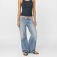 A model wearing the Luna super low in light indigo-wash denim, wide-leg Bubblegum jeans and a dark navy ribbed tank top, standing against a plain light gray studio background.