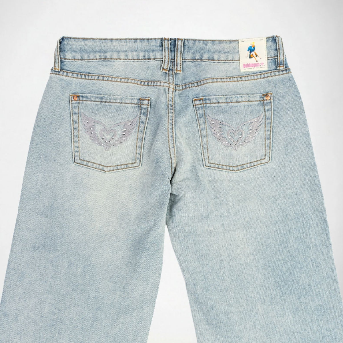 Back view of light-wash blue Bubblegum jeans featuring embroidered love wings with rhinestones on both back pockets and a Bubblegum USA brand patch on the waistband.