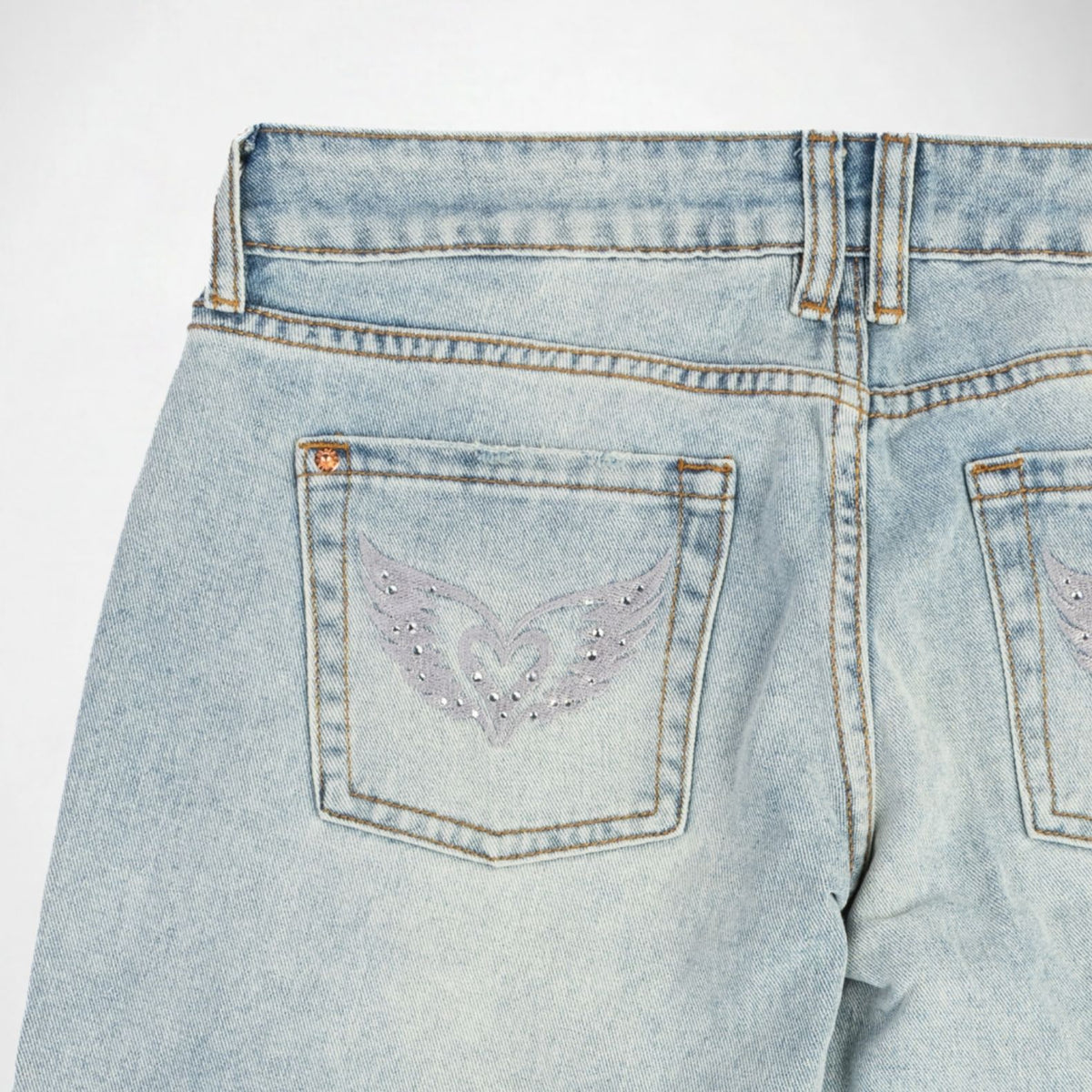 Close-up back view of light-wash blue denim Bubblegum jeans showing the back pockets with silver color thread embroidered with rhinestones and rivet details.
