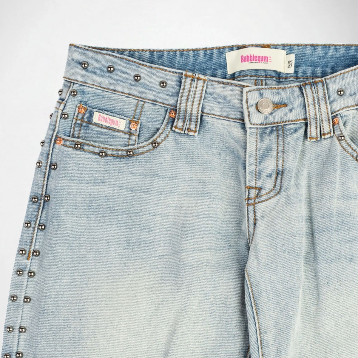 Close-up of a pair of light-wash blue denim Bubblegum jeans with silver metal studs along the side seams and pocket edges, featuring a Bubbleum USA brand label.