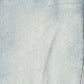 A close-up of light blue denim fabric texture with subtle fading and a diagonal seam visible on the right edge.