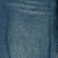 A close-up of blue denim fabric texture with subtle folds and a small portion of orange-brown stitching visible at the bottom right corner.
