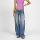 A model wearing a pair of Luna super low rise, wide-leg blue Bubblegum denim jeans with gold-tone studs down the outer seams, paired with a pink ribbed tank top and brown sandals, against a plain white studio background.