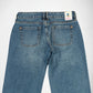Back view of a pair of blue denim Bubblegum jeans on a light gray background, showing the waistband, belt loops, two rear pockets, and a small colorful brand tag near the back right waistband.